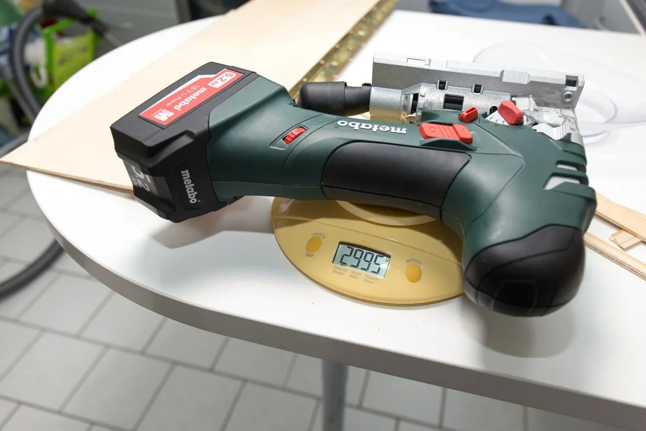Die Metabo Stichsäge liegt auf einem weißen Tisch auf einer gelben Waage. Die Waage zeigt 2995g an.
